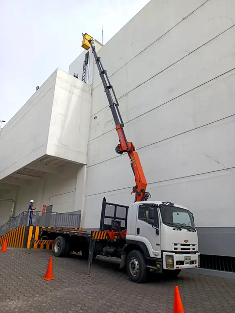 Camión grúa con el brazo extendido junto a un edificio