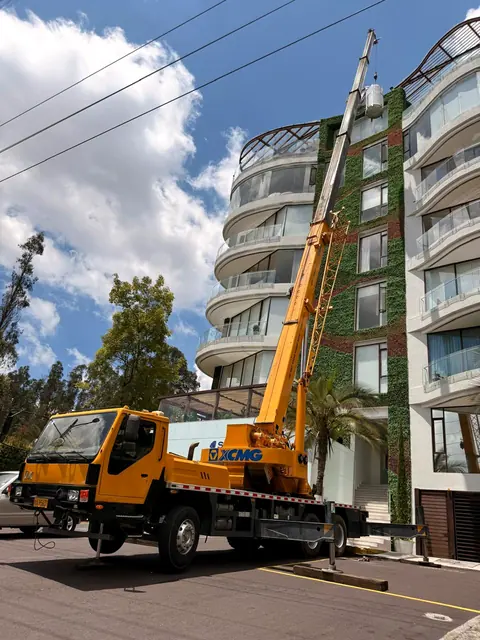 Grúa telescópica amarilla izando un tanque junto a un edificio