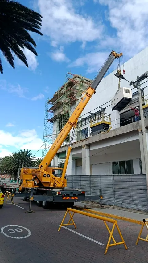 Grúa telescópica amarilla trabajando junto a un edificio en construcción
