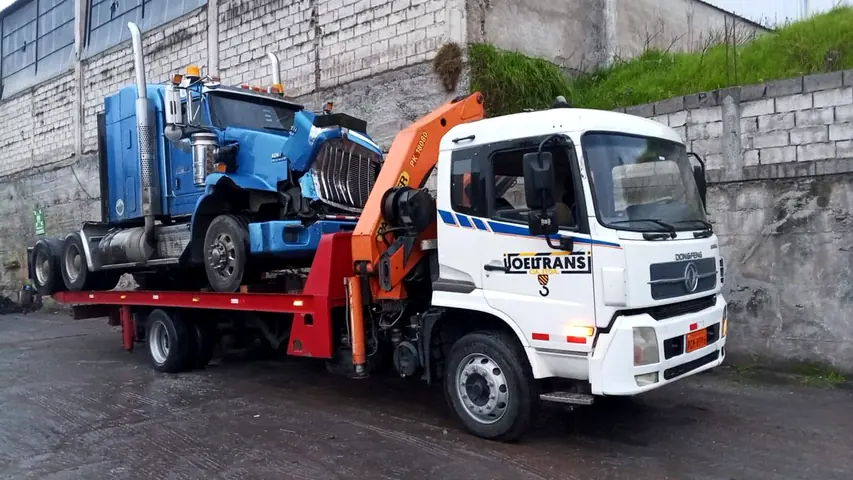 Plataforma autocargable con grúa trasladando un camión